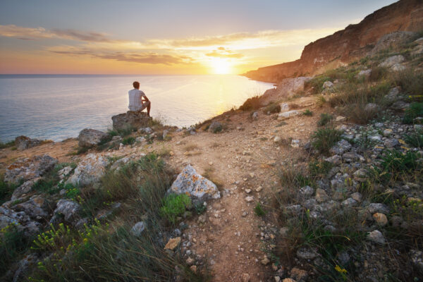 Man sitting on the rock cliff in mountain and watching on thr sunrise sea. Nature composition.