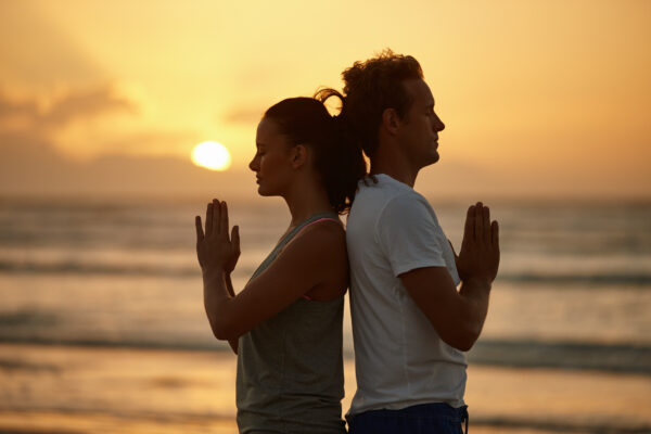 Soul experience at sunset. Shot of a couple doing yoga on the beach at sunset
